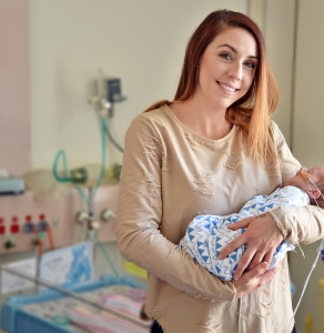 A young mother holding her newborn baby who has tubes coming from its nose.