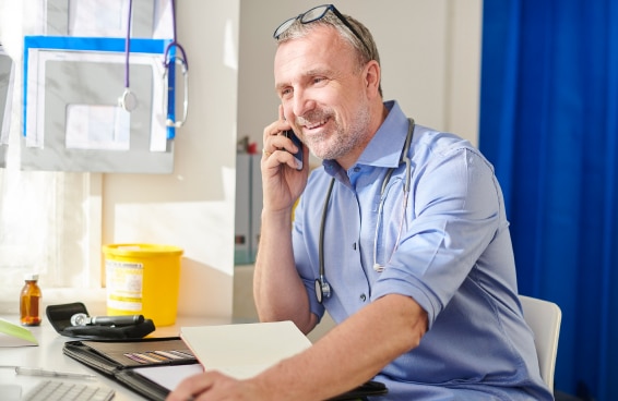 A health practitioner at his desk smiling while talking on the phone.