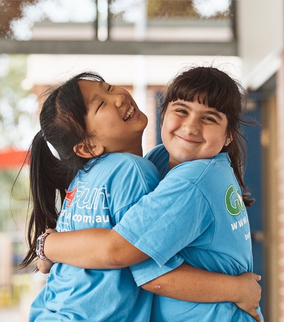 Two girls in Go4Fun t-shirts hugging and smiling at a Go4Fun session.