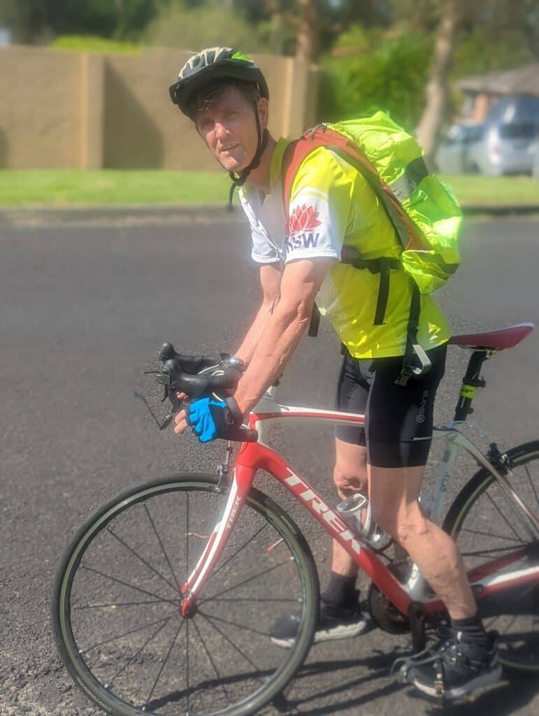 Greg Harris on his bicycle with a high-vis shirt and backpack on.