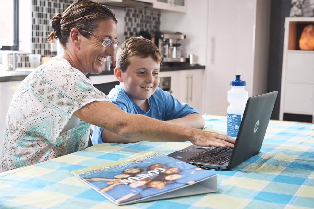 A mother and child at a laptop smiling with a Go4Fun water bottle and binder on the table.