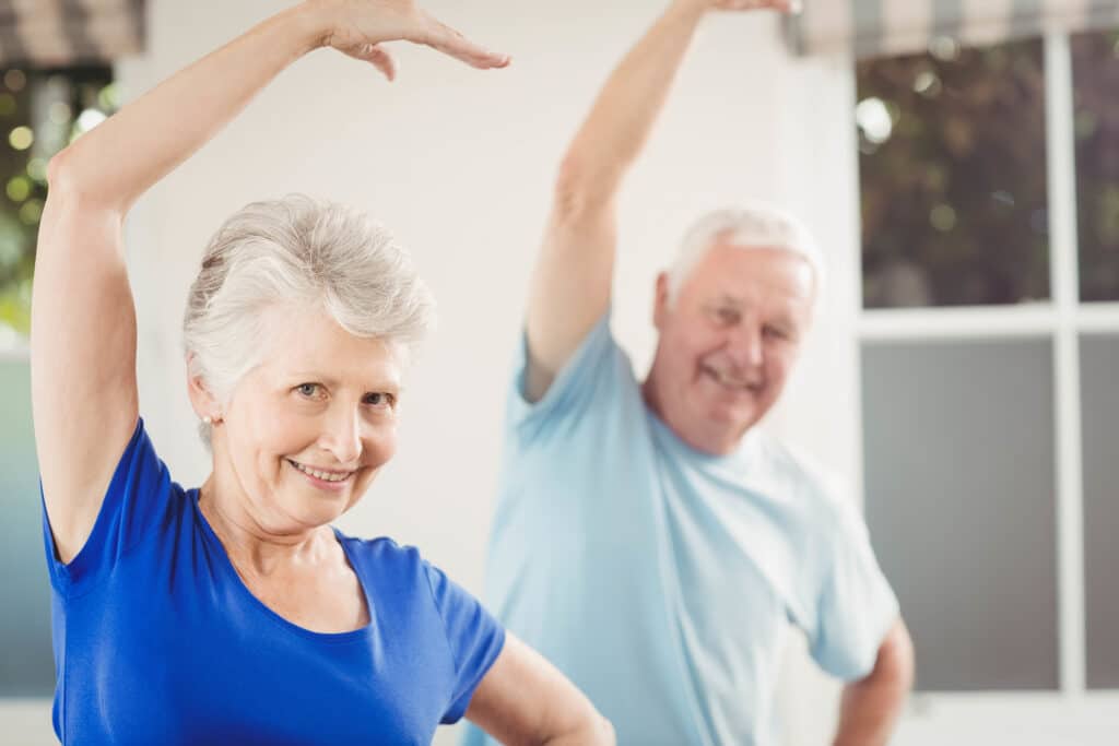 Older man and woman performing stretching exercise indoors.