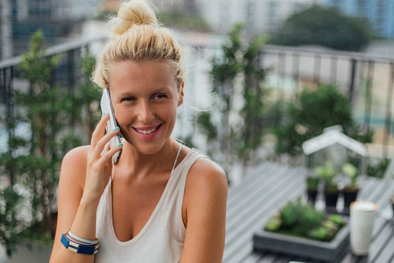 A young woman smiling on a balcony while talking on her mobile phone.