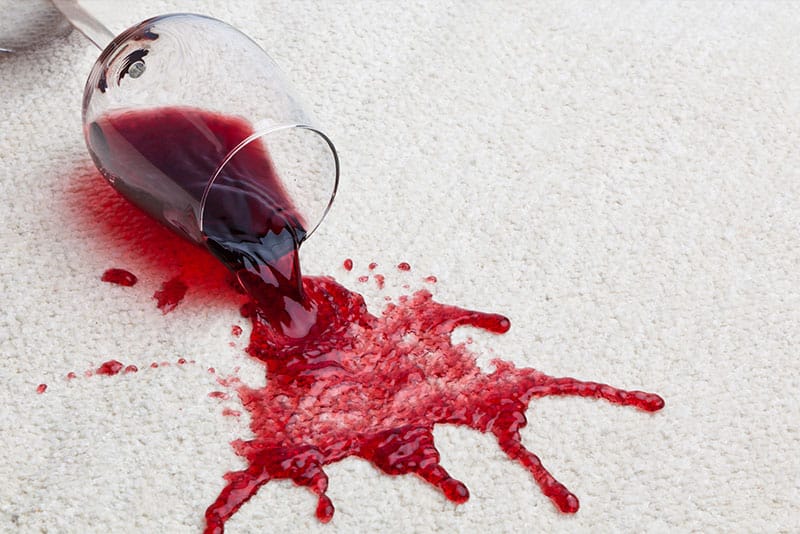 A wine glass knocked over and staining a light-coloured carpet.