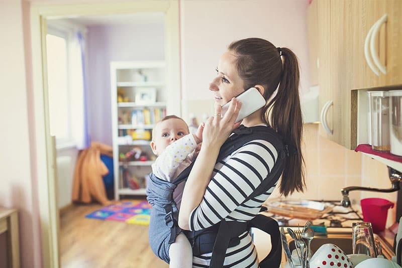 A young mum on the phone while her child is attached to her via a harness.