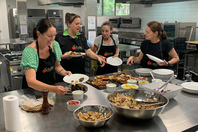 A group of canteen staff at a Canteen Network meeting chatting while preparing food.