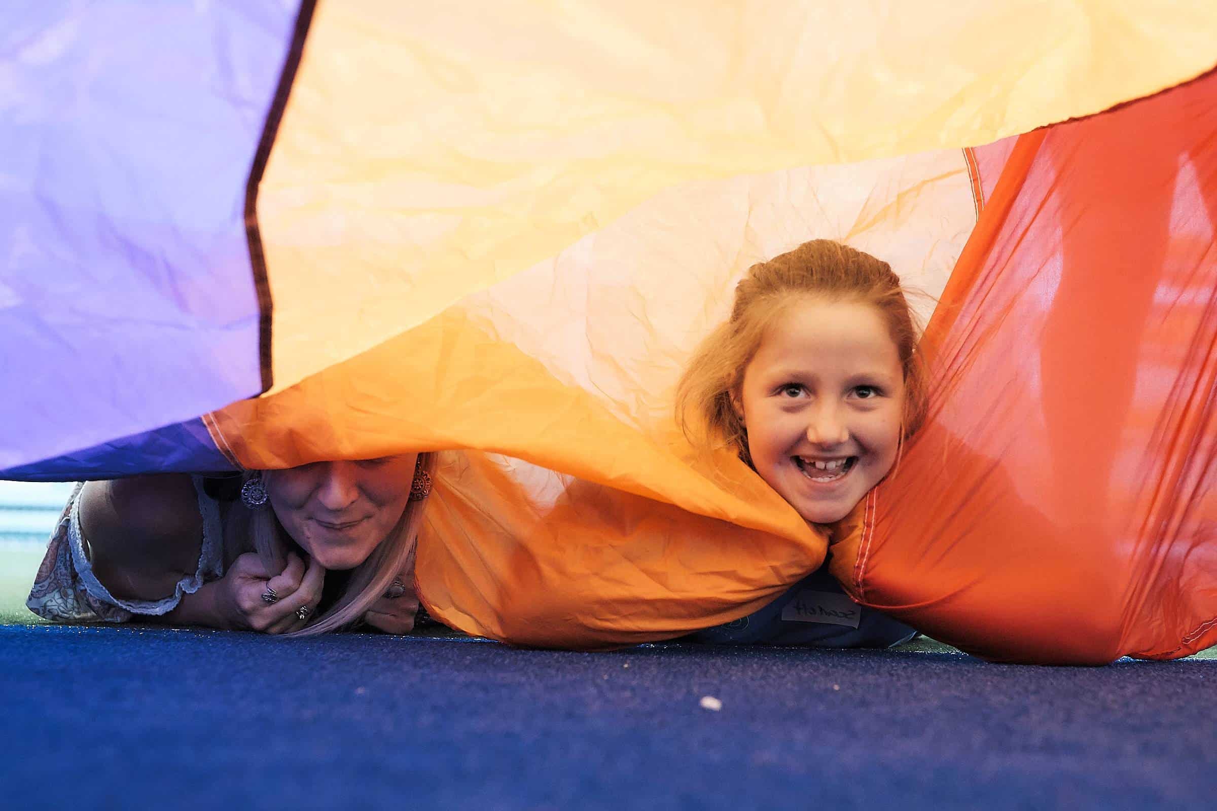 A girl and her mother under a parachute at a Go4Fun program.