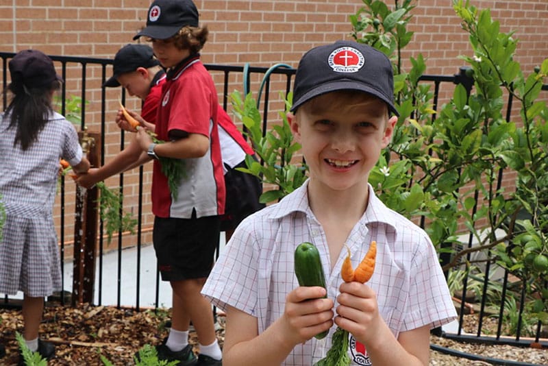 A student from Green Point Christian College holding vegetables from its garden.