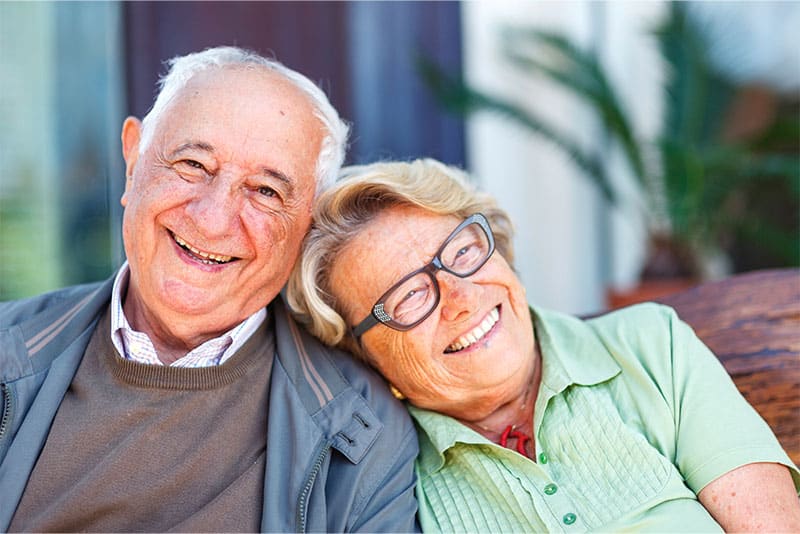 Two older adults sitting down outside smiling.