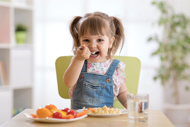 A young child eating healthy food at a table.
