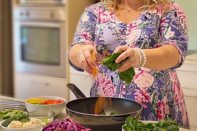 A pregnant lady throwing some vegetables into a wok.