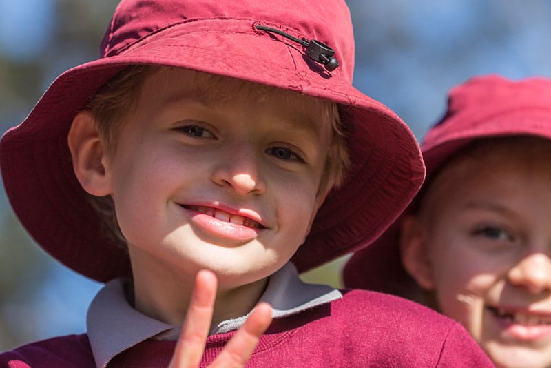 A young schoolboy in a hat smiling and giving the peace sign to the camera.