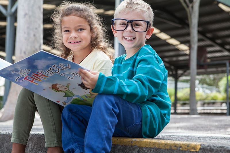 Two children dressed to look like the two main characters from Jack's FUNtastic Day hold the book open.