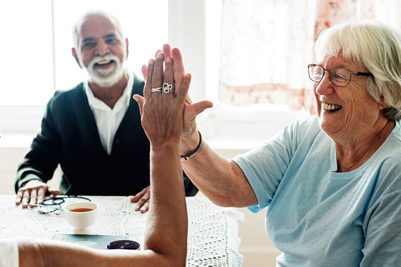 Two older adults give a high give as another looks on smiling.