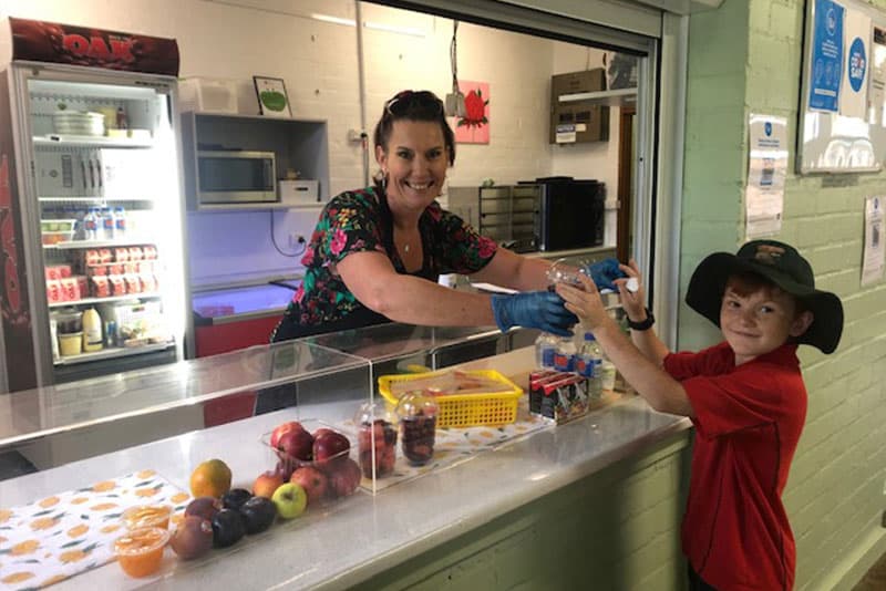 A school canteen staff member serving a young schoolboy.