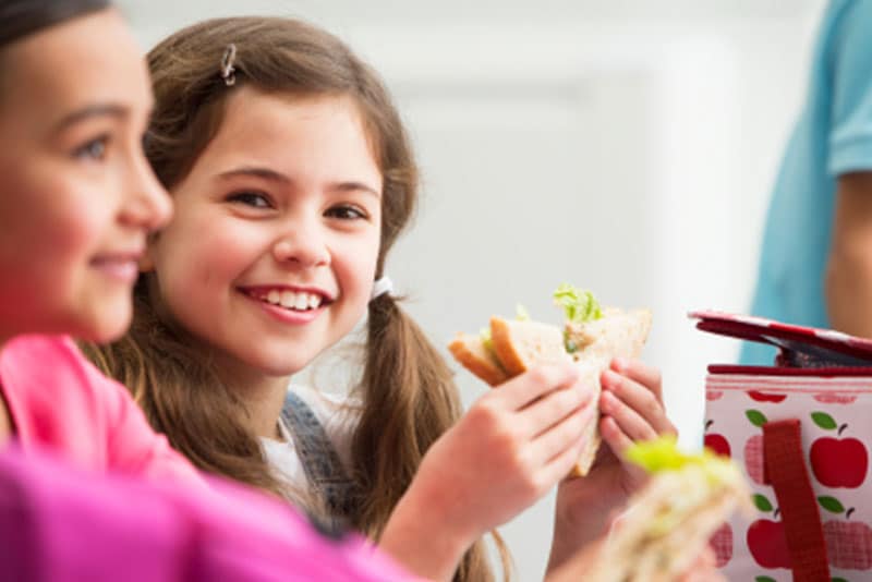 A young school girl eating a sandwich.