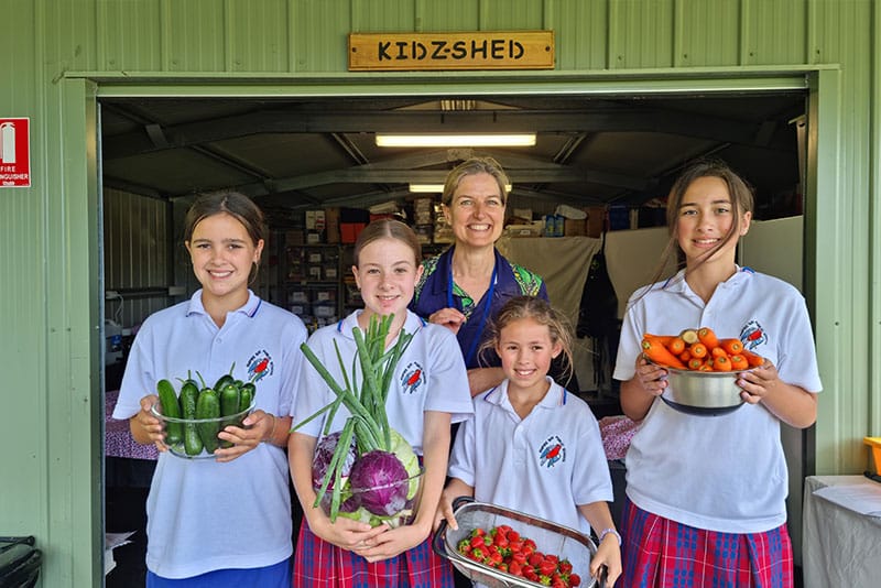 Four school children with their teacher showing off fruit and vegetables piking from their garden.