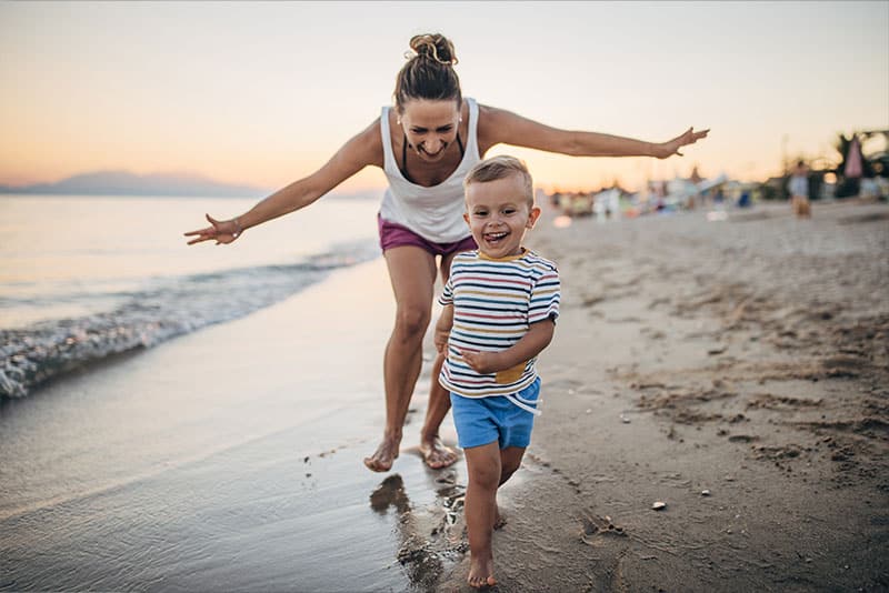 A young mother and young boy running along the beach smiling.