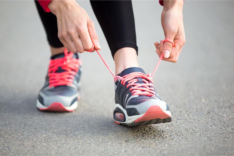 Two hands tying shoe laces on a pair of running shoes.