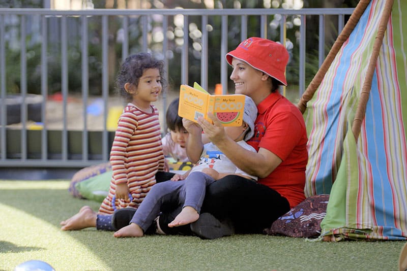 A early childhood educator reading a book to a child outside.