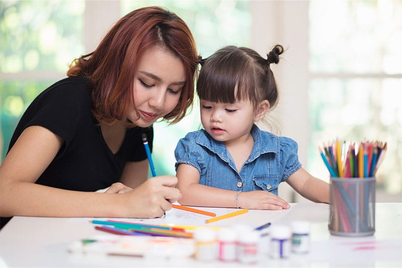 A young Asian mum drawing with her daughter.