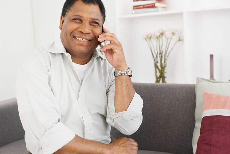 A black man smiling while talking on a mobile phone at home.