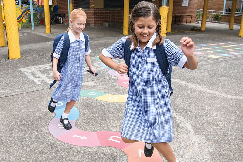 Two school girls smiling playing hop scotch in the playground.