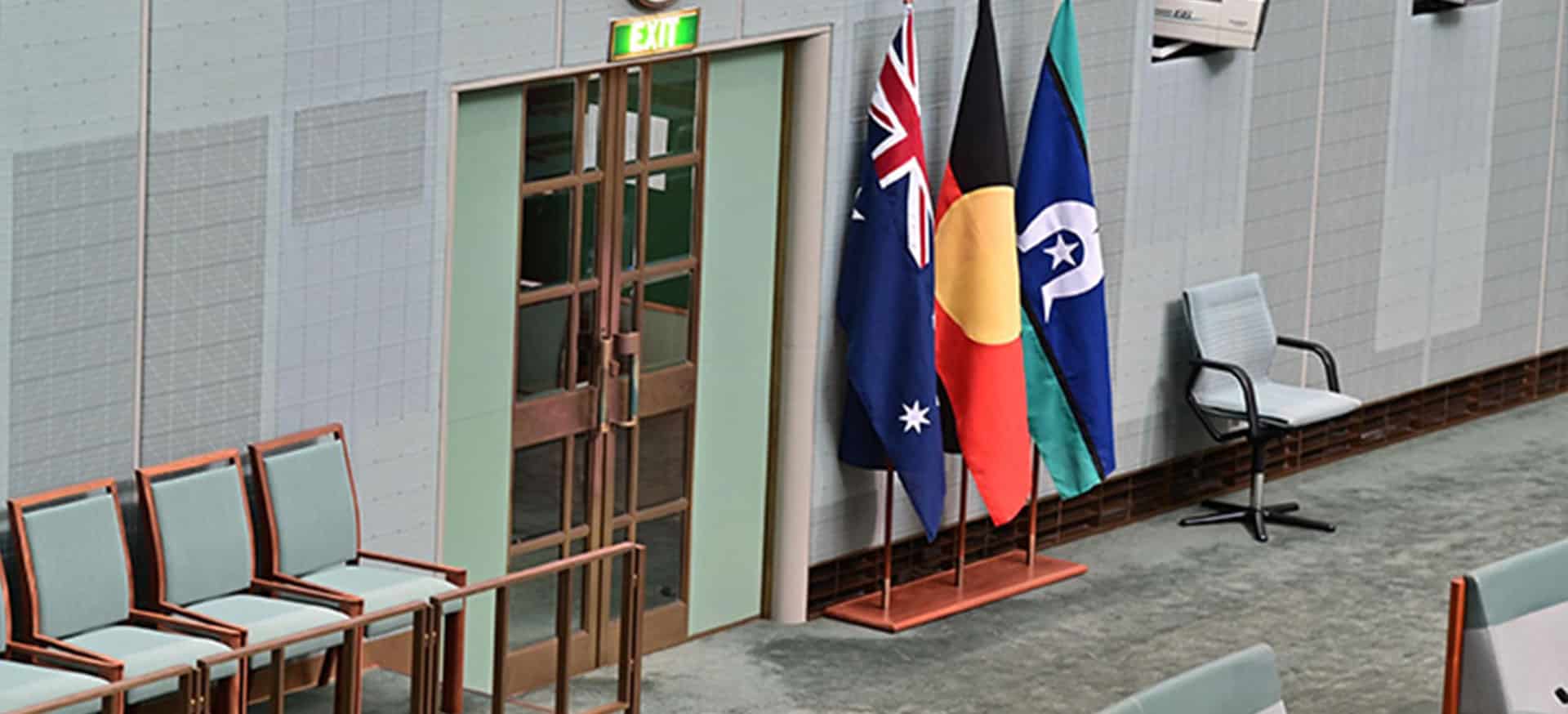 the Australian flag, Aboriginal flag and Torres Strait Islander flag at inside a parliamentary building.