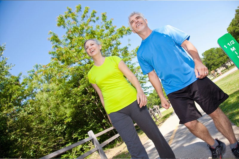 A man and woman smiling as they walk along a footpath in active wear.