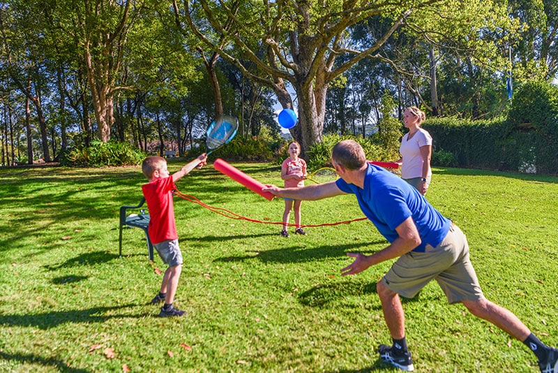 A family of four playing one of the Family ACTIVation games using a tennis racquet, foam stick and ball.