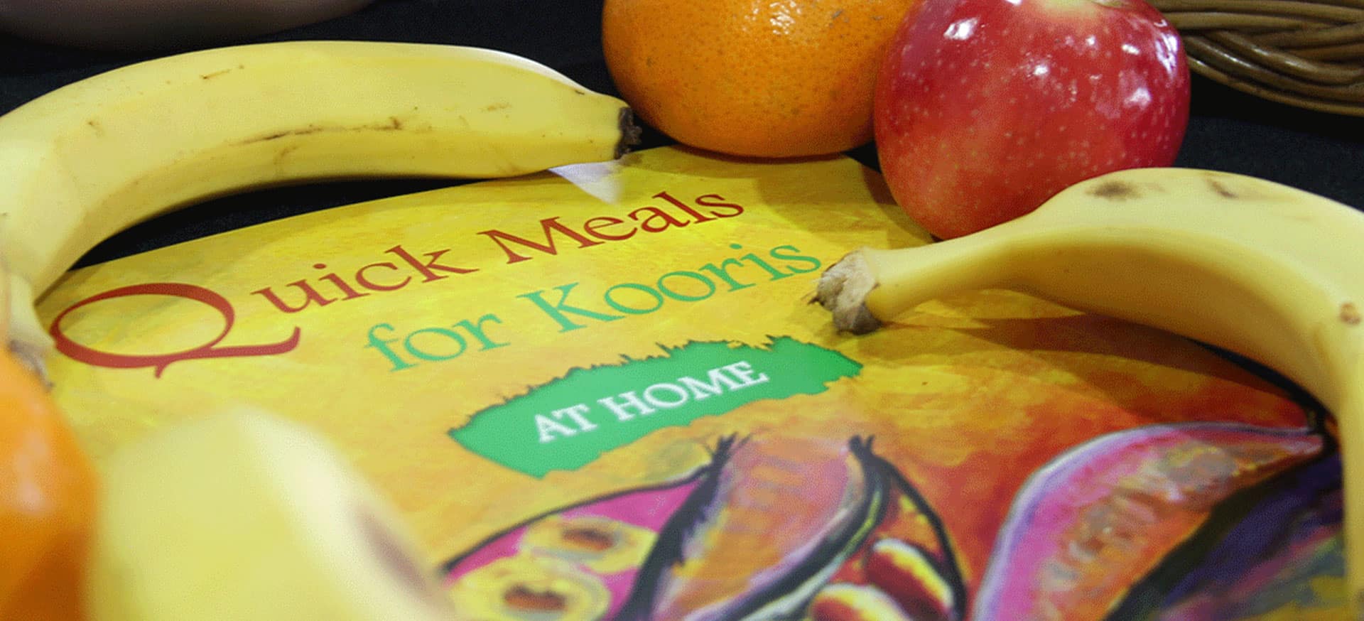 The Quick Meals for Kooris At Home manual with fruit laid on top.