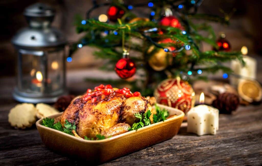 A roast chicken in front of a small Christmas tree.