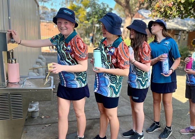 A line of school children filling up their refillable water bottles at a chilled water station.