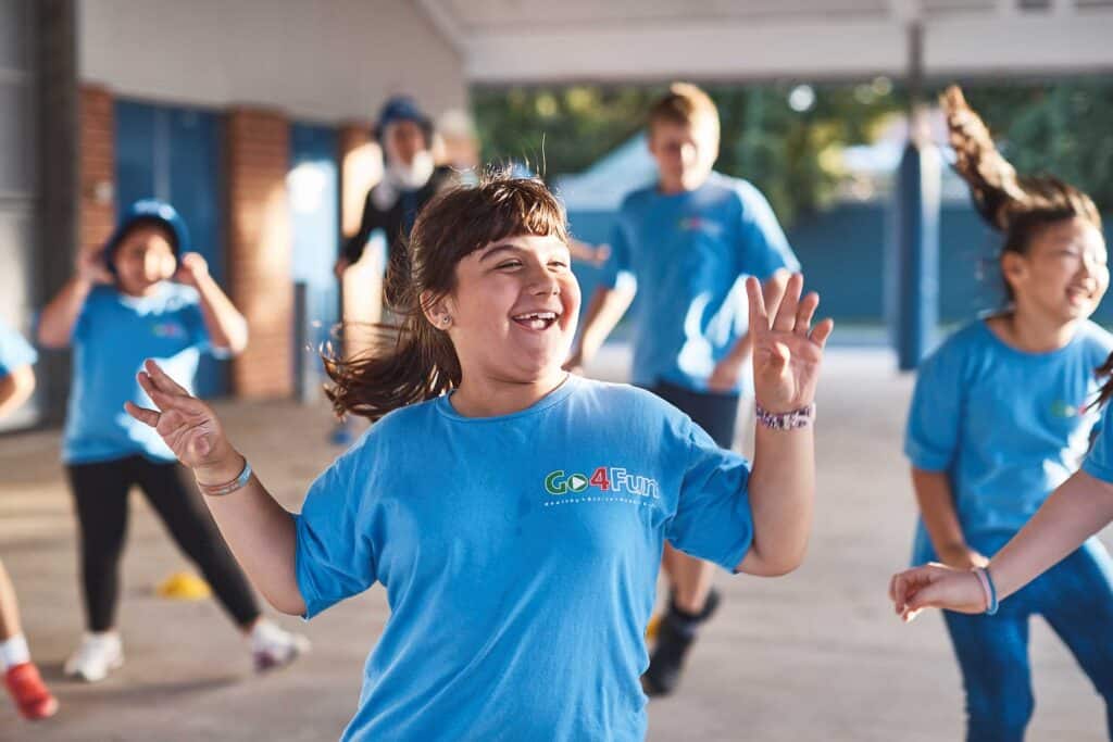 A girl dancing with a Go4Fun top on while a group of children dance behind her.