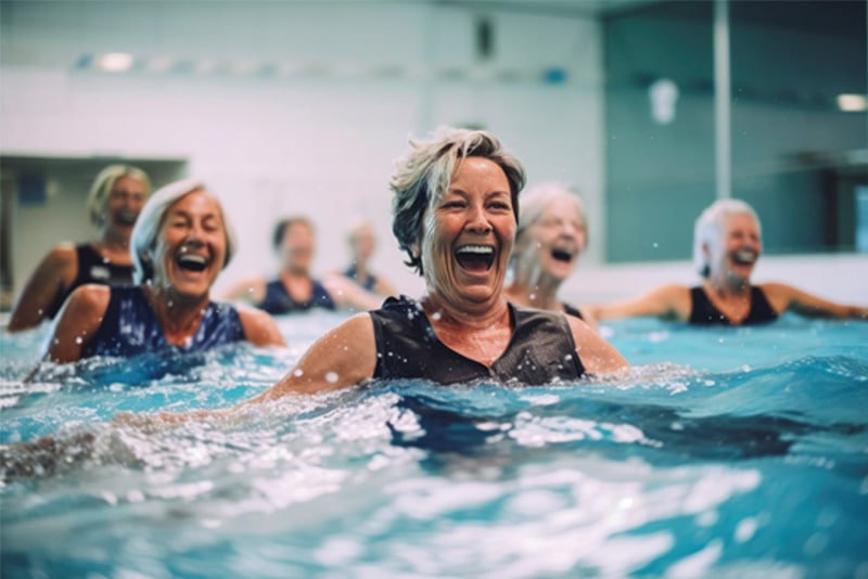 A group of women laughing while doing an exercise class in a swimming pool.