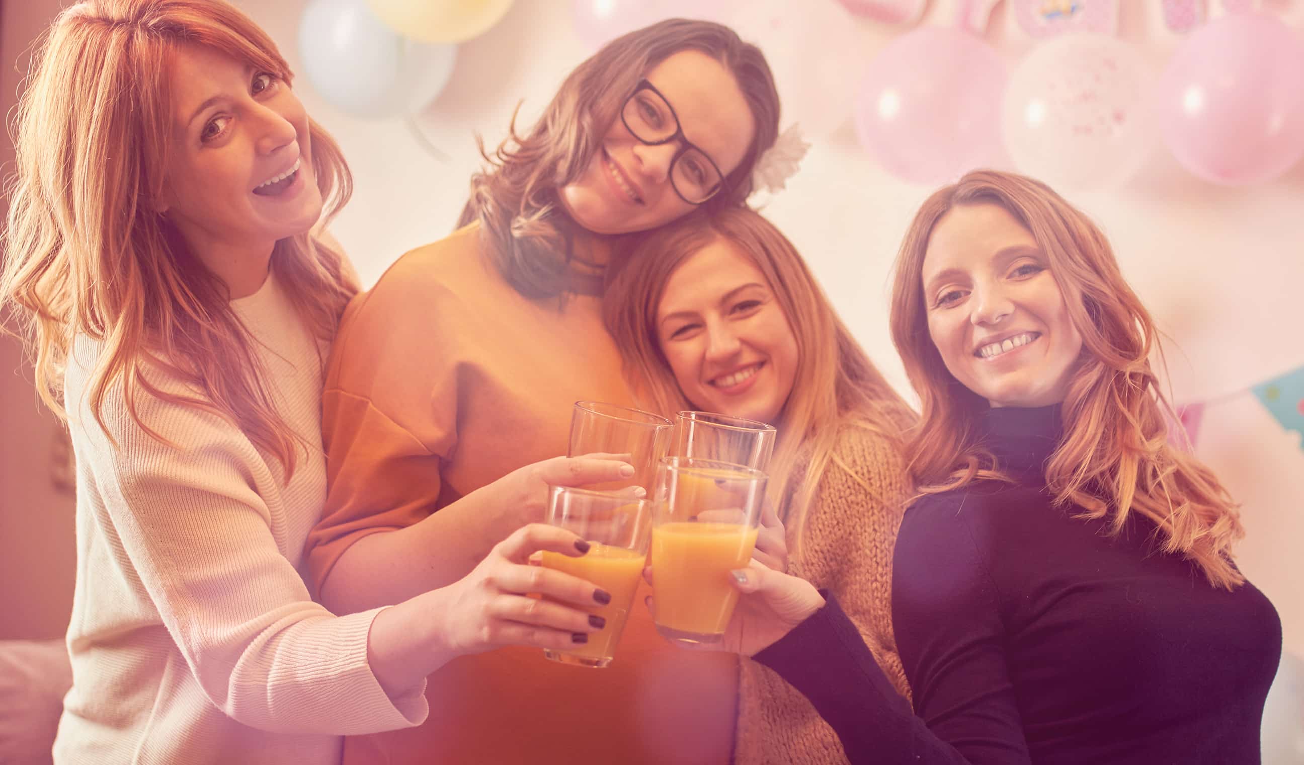 Pregnant woman celebrating baby shower party with glasses of orange juice.
