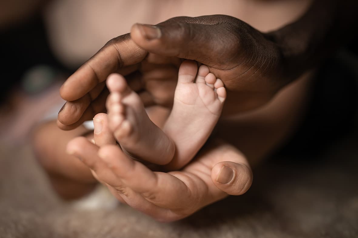 Interracial family holding baby feet in hands mixed by black and white skin color.