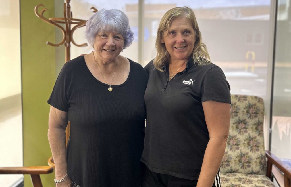An older adult stands next to her exercise class instructor smiling.