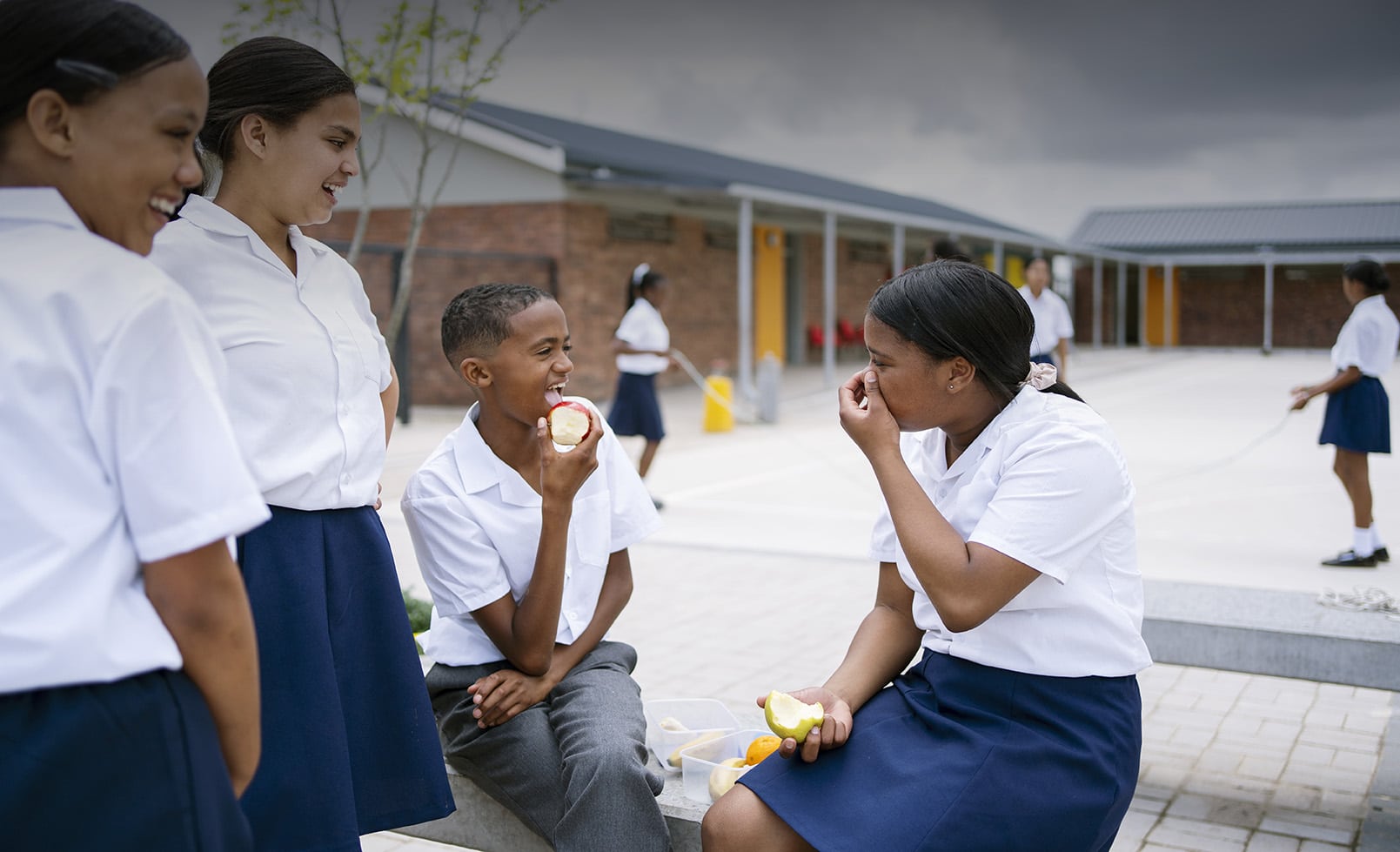 Group of happy school children having lunch together sitting outside in the campus