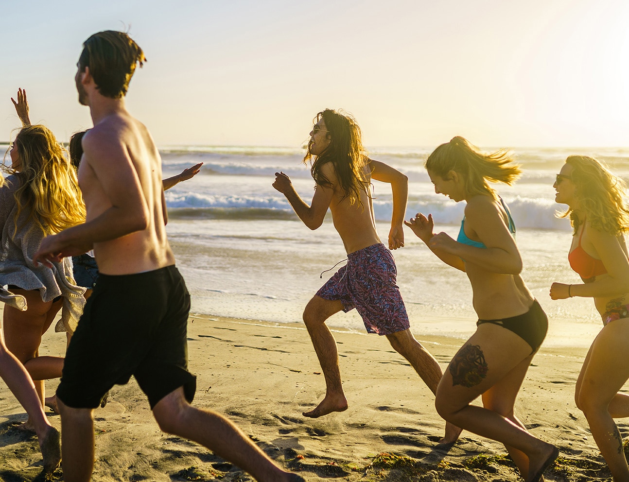 group of friends running alongside beach