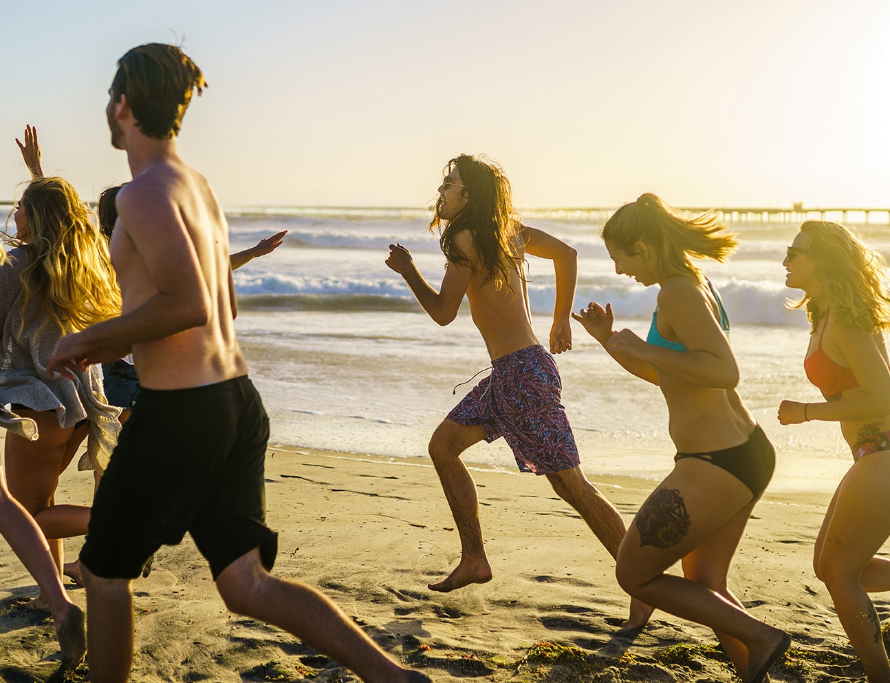 group of friends running alongside beach in california