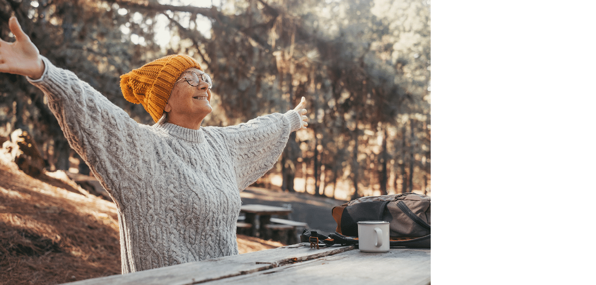 Head shot portrait close up of middle age woman enjoying and relaxing sitting at table in the nature in the forest of mountain. Old female person opening arms and closing eyes feeling free. Freedom 